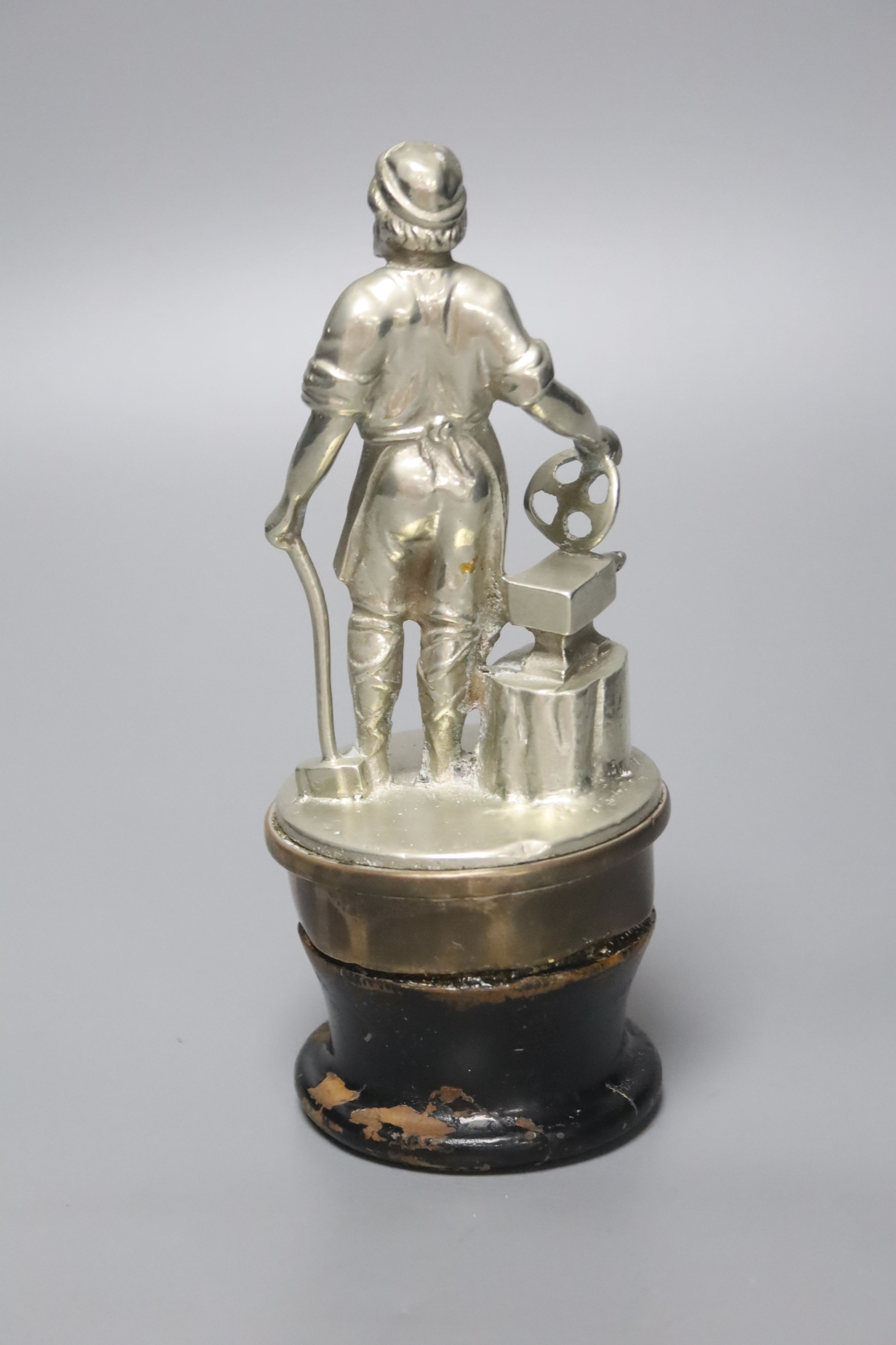 A large cast metal Vulcan car mascot, in the form of a blacksmith, on brass base and lacquered wooden socle, 18cm high